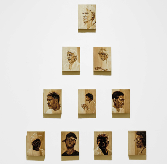 Natalie Erin Brown, Value Pyramid, Wood burnings, 2015. 10 individual wood burnings depicting portraits of people with skin tones ranging from dark to white and arranged in a pyramid formation with black at the bottom and white at the top.