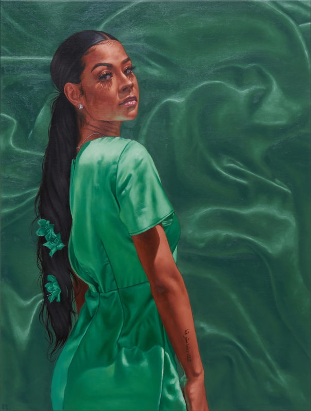 Portrait of a woman looking over her shoulder toward the viewer. She is in a satin green dress, and the background mimics the material and color of the fabric of her dress.